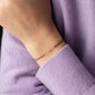 Armband aus Stoff in Beige mit 18 KT Roségoldenen Gliedern an Handgelenk von Person in lila Pullover