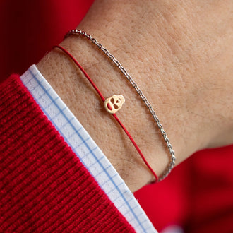 Handgelenk mit rotem Pullover und Hemdärmel mit Armkette SAM Petite in Silber und Armband SKULL in Gelbgold mit rotem Stoffband
