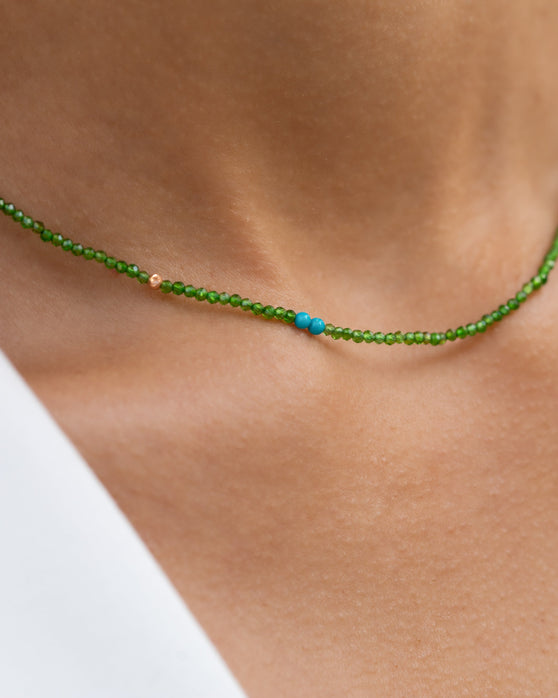 Kurze, gruene Halskette mit Edelsteinen aus 18 KT Roségold. Halskette mit Chromdiopsiden und Türkisen – ein sommerliches Schmuckstück von ANNA. Getragen am Hals einer Frau, Nahaufnahme der Kettendetails.