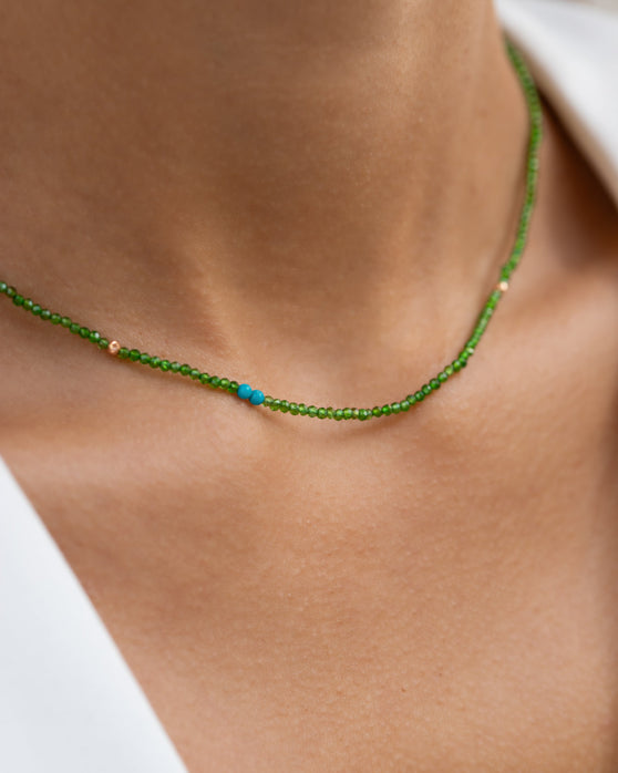 Kurze, gruene Halskette mit Edelsteinen aus 18 KT Roségold. Halskette mit Chromdiopsiden und Türkisen – ein sommerliches Schmuckstück von ANNA. Getragen am Hals einer Frau mit weißem Blazer.