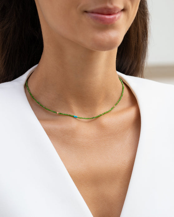 Kurze, gruene Halskette mit Edelsteinen aus 18 KT Roségold. Halskette mit Chromdiopsiden und Türkisen – ein sommerliches Schmuckstück von ANNA. Getragen am Hals einer Frau mit schwarzen Haaren und weißem Blazer.