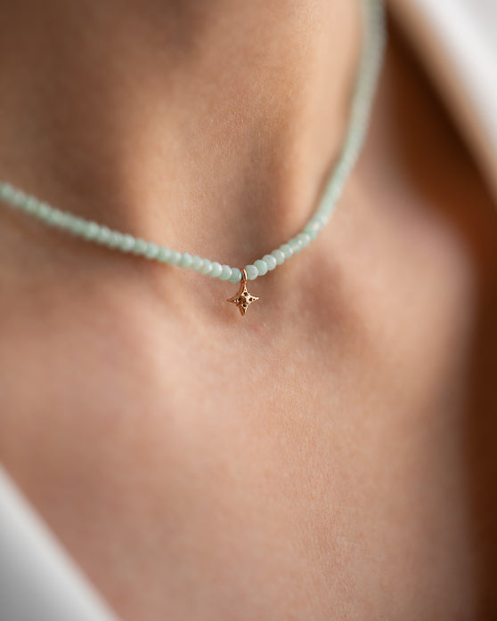 Kurze, blassgrüne Halskette mit Edelsteinen aus 18 KT Roségold. Halskette TAMI mit Chrysopras und Stern-Anhänger – ein sommerliches Schmuckstück von ANNA. Getragen am Hals einer Frau - Detailaufnahme.