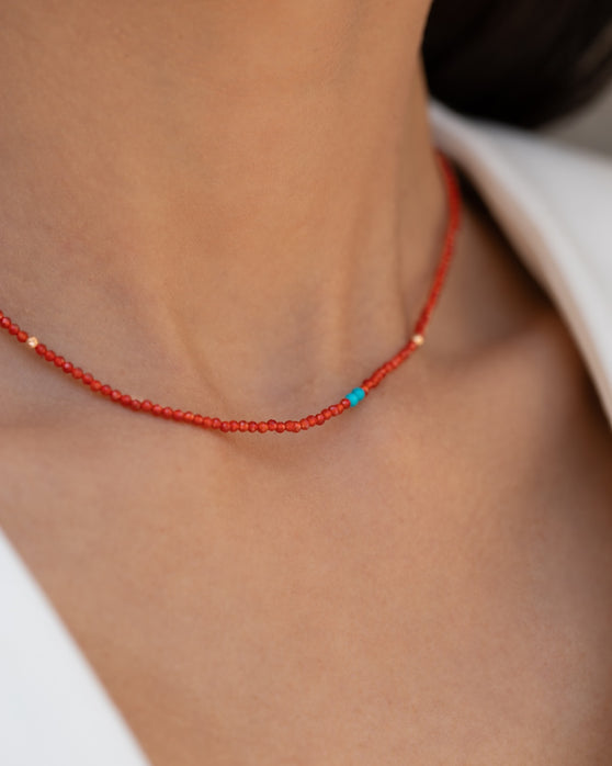 Kurze, rote Halskette mit Edelsteinen aus 18 KT Roségold. Halskette mit Karneolen und Türkisen – ein sommerliches Schmuckstück von ANNA. Getragen am Hals einer Frau mit schwarzen Haaren und weißem Blazer. Detailaufnahme.