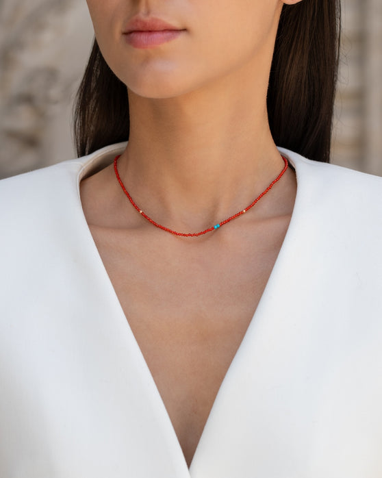 Kurze, rote Halskette mit Edelsteinen aus 18 KT Roségold. Halskette mit Karneolen und Türkisen – ein sommerliches Schmuckstück von ANNA. Getragen am Hals einer Frau mit schwarzen Haaren und weißem Blazer.