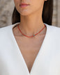 Kurze, rote Halskette mit Edelsteinen aus 18 KT Roségold. Halskette mit Karneolen und Türkisen – ein sommerliches Schmuckstück von ANNA. Getragen am Hals einer Frau mit schwarzen Haaren und weißem Blazer.