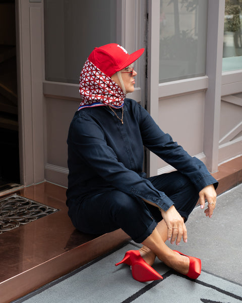 Rotes Seidentuch mit blau-weißem Muster als stilvolles Accessoire am Kopf getragen von einer blonden Frau mit roten Schuhen und dunkelblauem Jumpsuit.