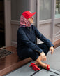 Rotes Seidentuch mit blau-weißem Muster als stilvolles Accessoire am Kopf getragen von einer blonden Frau mit roten Schuhen und dunkelblauem Jumpsuit.