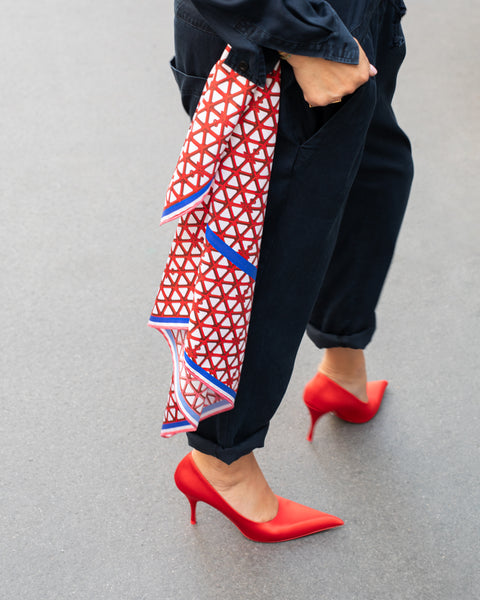 Rotes Seidentuch mit blau-weißem Muster als stilvolles Accessoire an der Hose getragen von einer Frau mit roten Schuhen und dunkelblauem Jumpsuit.