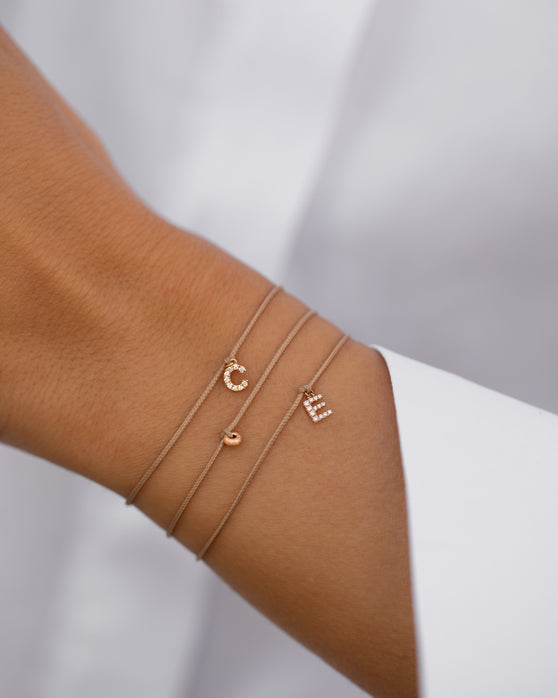 Drei personalisierte Armbänder aus 18 KT Roségold von ANNA mit Initialen und Buchstaben-Anhänger mit Diamanten. Individueller Schmuck zum Kombinieren für Dein Armcandy. Getragen am Handgelenk von einer Frau mit weißer Bluse.