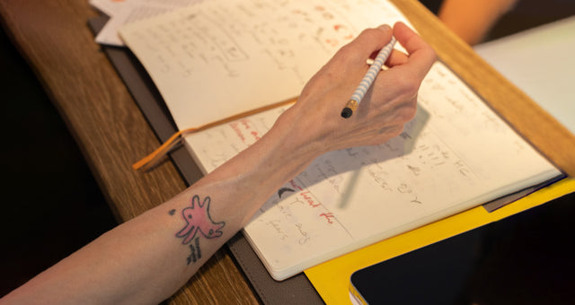 Hand mit Stift und Notizbuch mit Tattoo von rosa Uranian Rabbit