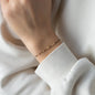 Armband mit beigem Stoffband und sechs verschobenen goldenen Perlen an Handgelenk mit weißem Ärmel