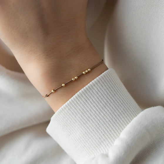 Nahaufnahme von Armband LANA in Gelbgold mit kleinen Perlen und beigem Stoffband getragen an Handgelenk