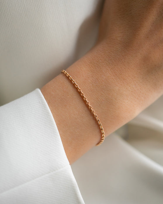 Eine schlichte Armkette aus Roségold ohne Anhaenger. Feine Gliederkette, die nicht zu grob ist und nicht zu zart. Getragen an einem Frauenhandgelenk.