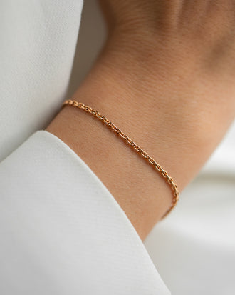 Eine schlichte Armkette aus Roségold ohne Anhaenger. Feine Gliederkette, die nicht zu grob ist und nicht zu zart. Getragen an einem Frauenhandgelenk.