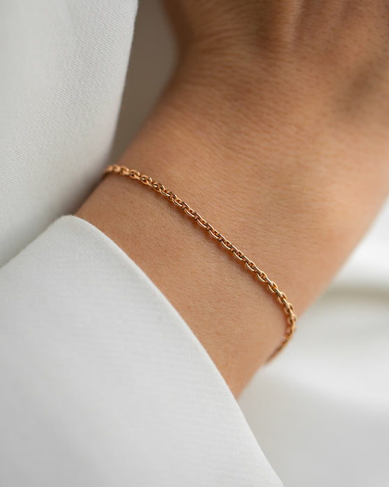 Eine schlichte Armkette aus Roségold ohne Anhaenger. Feine Gliederkette, die nicht zu grob ist und nicht zu zart. Getragen an einem Frauenhandgelenk.