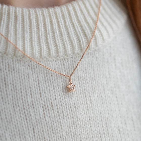 Zarte Halskette mit Stern-Anhänger in 18 KT Rosegold mit weißen Diamanten getragen von Frau in weißem Pullover