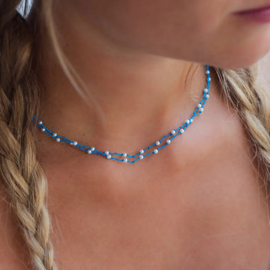 Stoffhalskette in Blau mit vielen kleinen weißen Perlen getragen an Hals von Frau