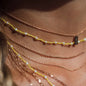 Nahaufnahme von Hals mit vielen Halsketten in Roségold und Stoffband in Sonnengelb mit weißen Perlen