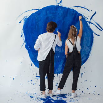 Mann und Frau in Latzhose am malen mit blauer Acrylfarbe