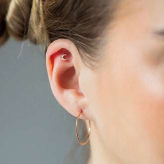 Nahaufnahme von Ear Piercing LUNA in Mondform, mit weißen Diamanten und in 18 KT Rosegold getragen an Ohr von Frau