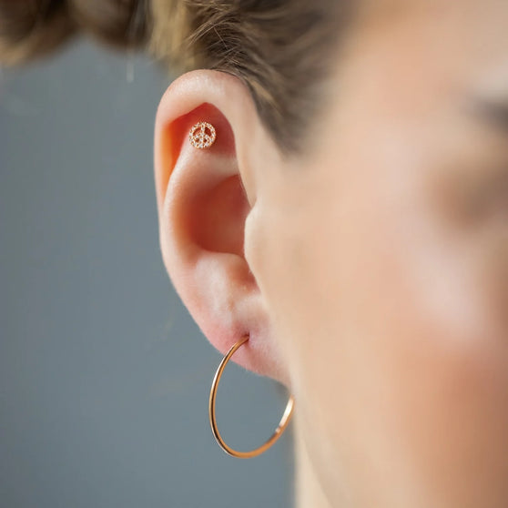Ear Piercing PEACE mit Peace-Zeichen, mit weißen Diamanten und in 18 KT Rosegold getragen an Ohr von Frau