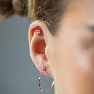 Ear Piercing PEACE mit Peace-Zeichen, weißen Diamanten und in 18 KT Rosegold getragen an Ohr von Frau