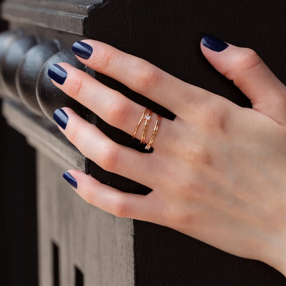 Nahaufnahme von Hand von Frau mit blauem Nagellack und zarten Ringen aus 18 KT Roségold mit weißen Diamanten in Baguette Schliff