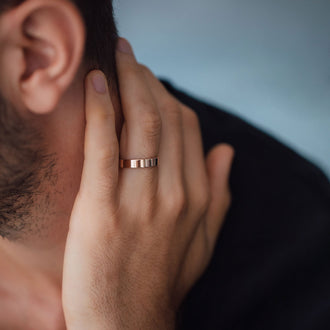 Mann mit rosegoldenem Ehering an Finger streicht sich über seinen Nacken