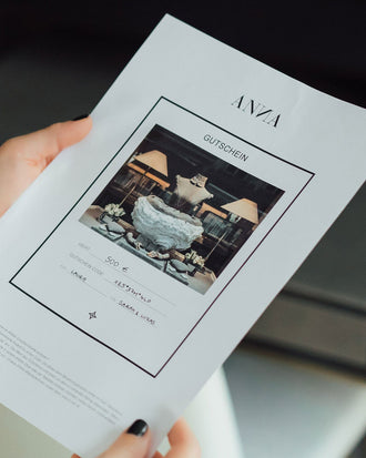 ausgedruckter E-Mail Geschenk Gutschein von ANNA  mit Wert 500 Euro in Händen von Frau mit schwarzem Nagellack