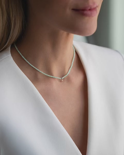 Kurze, blassgrüne Halskette mit Edelsteinen aus 18 KT Roségold. Halskette TAMI mit Chrysopras und Stern-Anhänger – ein sommerliches Schmuckstück von ANNA. Getragen am Hals einer Frau mit blonden Haaren und weißem Blazer.