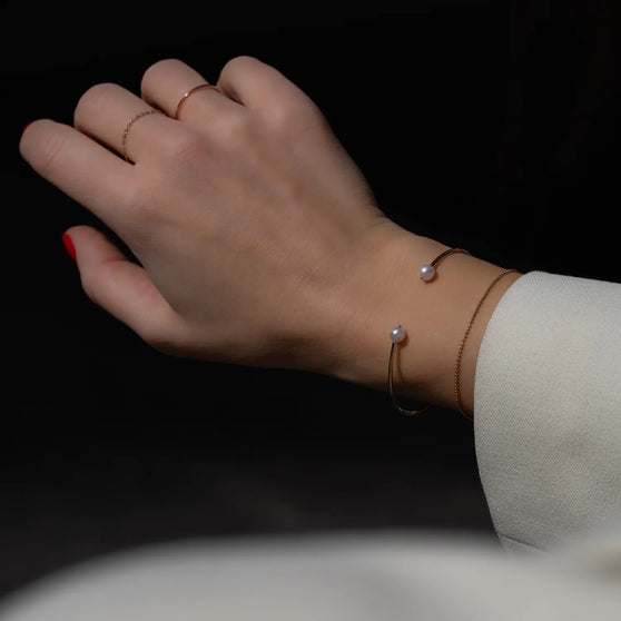 Hand mit zarten Ringen in Roségold und Armreif WAVE in Roségold mit weißen Akayo Perlen und filigraner Goldarmkette am Handgelenk