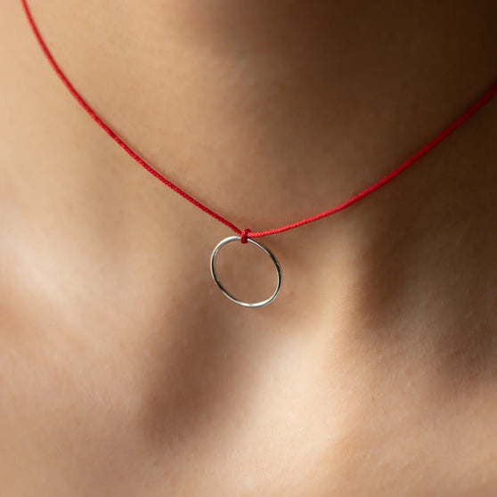 Nahaufnahme von Halskette LEXI mit rundem Silberanhänger und rotem Stoffband getragen von Frau