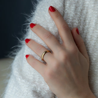 Hand vor weißem Fellhintergrund mit Ehering Beloved in Gelbgold und rot lackierten Fingernägel