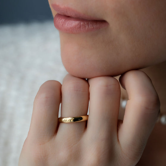 Frau stützt Kinn an Hand ab mit Ehering Beloved in Gelbgold an Ringfinger