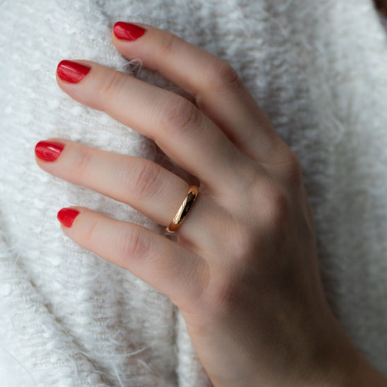 Frauenhand mit rot lackierten Fingernägel und roségoldenem Ehering an Ringfinger