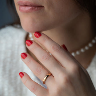 Frau mit Hand an Kinn mit rot lackierten Fingernägel, Perlenkette und Ehering Beloved in Roségold