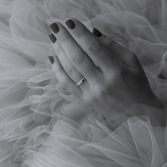 Hand in Tüll mit glänzendem Ehering an Ringfinger in schwarz weiß
